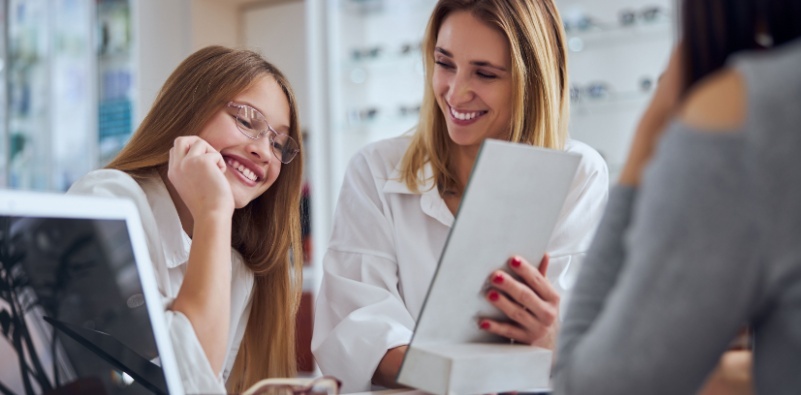 A mother and daughter choosing and trying different eyeglasses at the eye doctor’s
