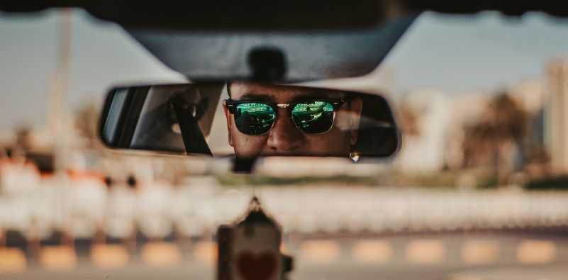 A man captured wearing sunglasses whilst driving through the car mirror