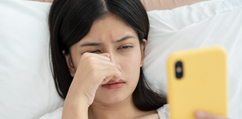 Woman rubbing her right eye while using a smartphone