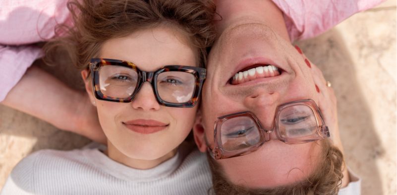 Two people lying side by side wearing bold, oversized glasses